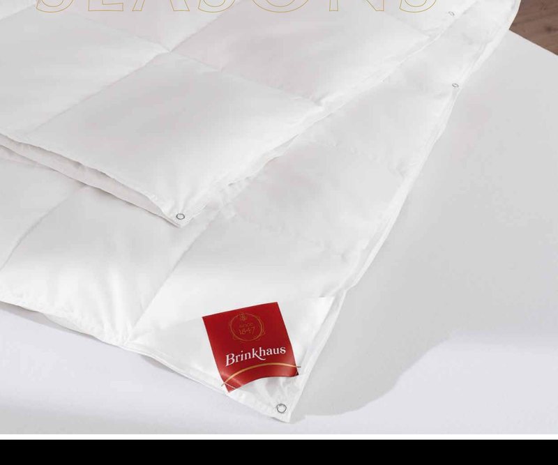 Сложенное белое одеяло FOR ALL SEASONS на кровати, угол с биркой Brinkhaus