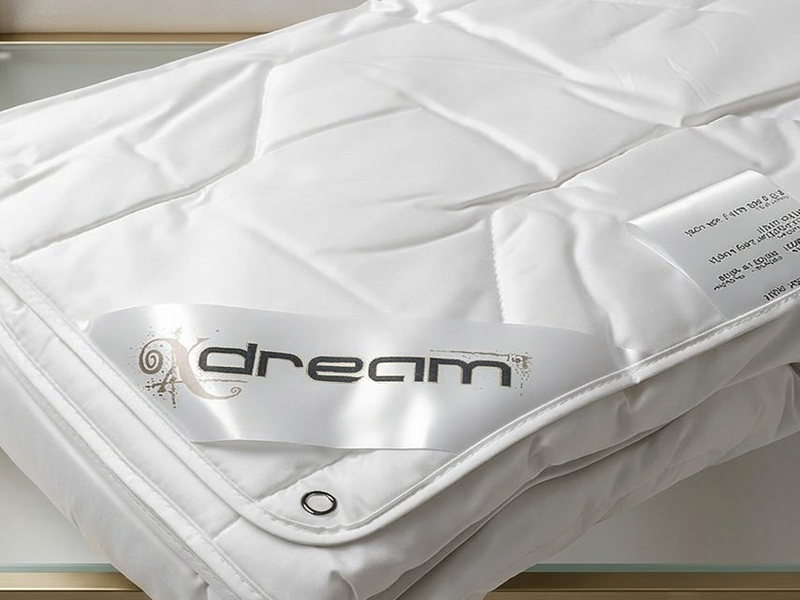 Белое стёганое одеяло Dreaming на стеклянной полке, на канте атласная бирка X-DREAM и бирка состава