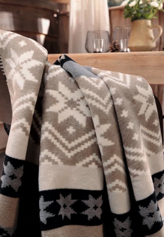 Плед Biederlack WINTER BRAID сложен складками на столе, видны полосы со звёздным орнаментом