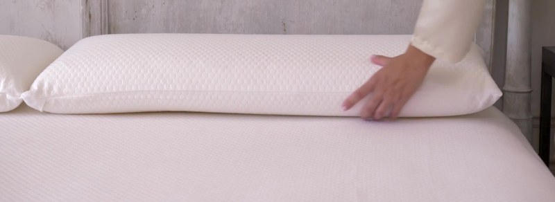 Подушка B-Sensible COSMETIC со стёганым чехлом лежит на кровати, рука поправляет угол — виден рельеф стёжки