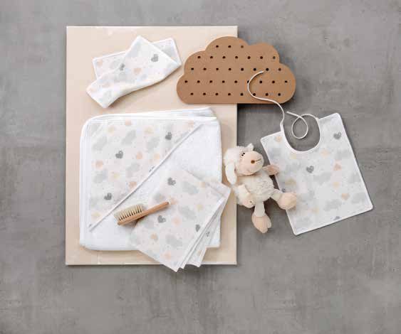 Изделия Feiler Mini LOVELY SKY разложены на серой поверхности: полотенце, салфетка, нагрудник и салфетка с игрушкой — белое поле с серыми облачками и сердечками; рядом деревянная щётка и плюшевый зверёк